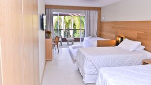 Ein Hotelzimmer mit zwei Betten, einem Schreibtisch und einem Stuhl. Ein großes Fenster mit Vorhängen bietet Blick auf Grünflächen.
