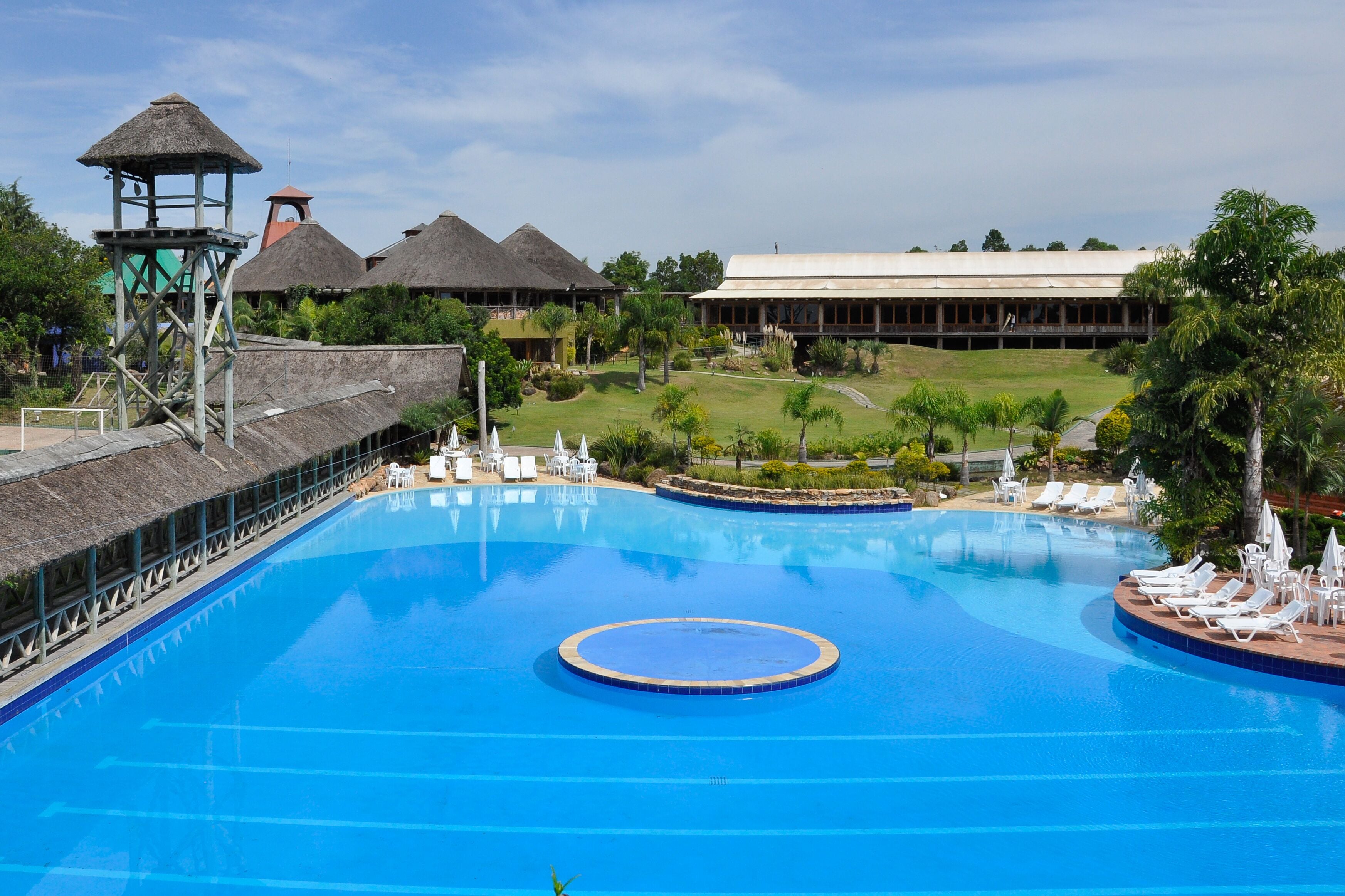 A large swimming pool with lounge chairs and a thatched-roof structure.