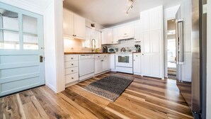 Una cocina moderna con gabinetes blancos, piso de madera y refrigerador de acero inoxidable.