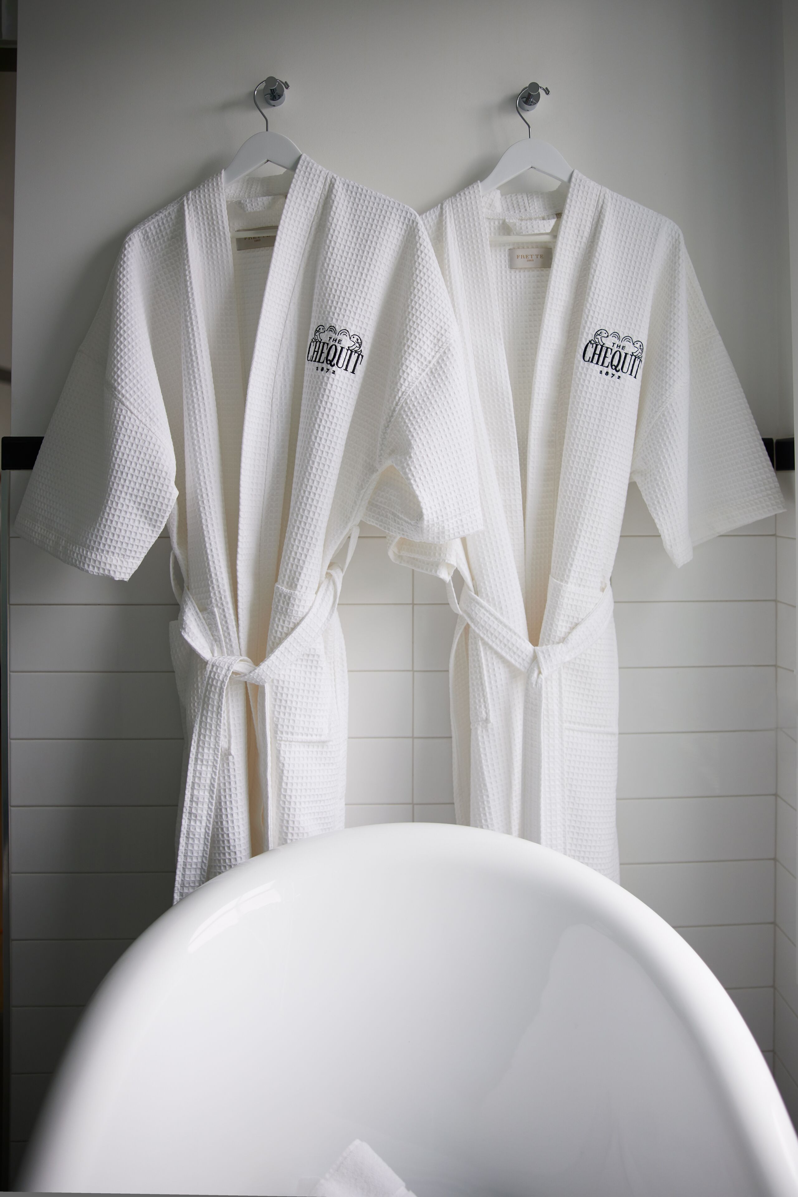 Two white robes with "The Chequilt" logo hanging on a wall.