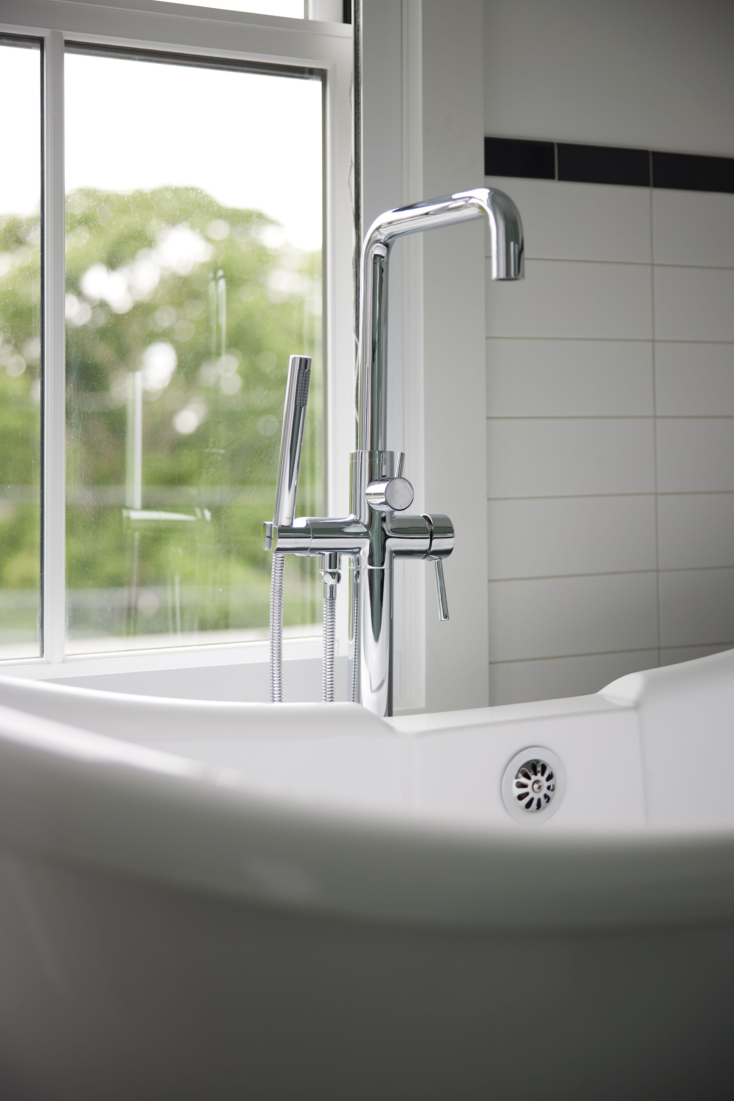 A modern bathroom with a bathtub, a chrome faucet, and a window providing a view of greenery outside.