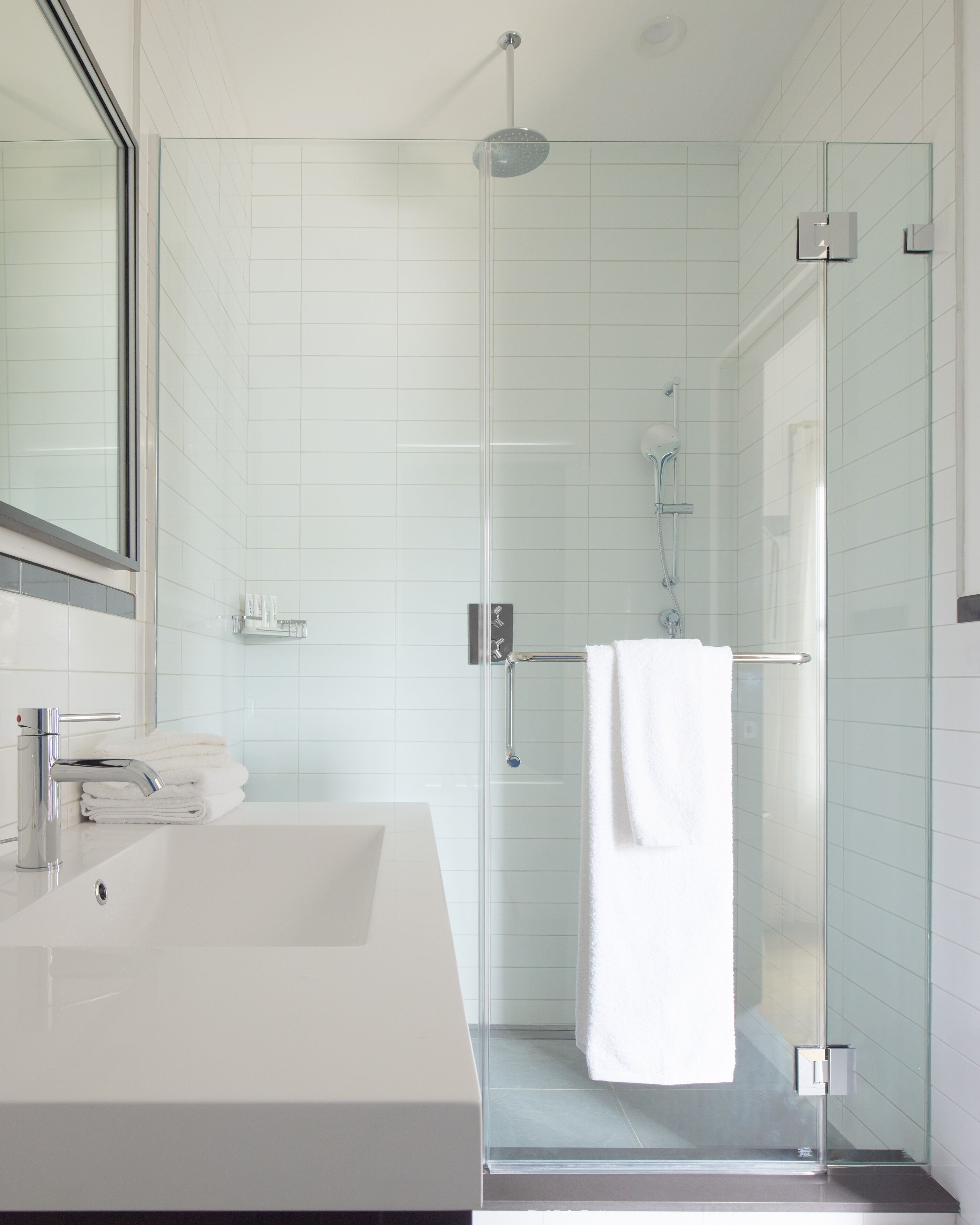 Een moderne badkamer met een douchecabine van glas, een witte wastafel en een spiegel erboven.