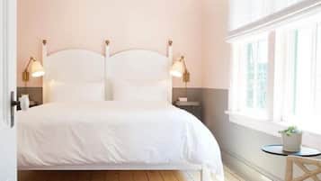 A neatly arranged bedroom with a double bed, bedside lamps, a small table with a plant, and a window with curtains.