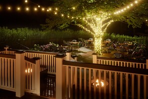 An outdoor patio area with string lights, tables, chairs, and a fire pit. - The Chequit (Shelter Island Heights)
