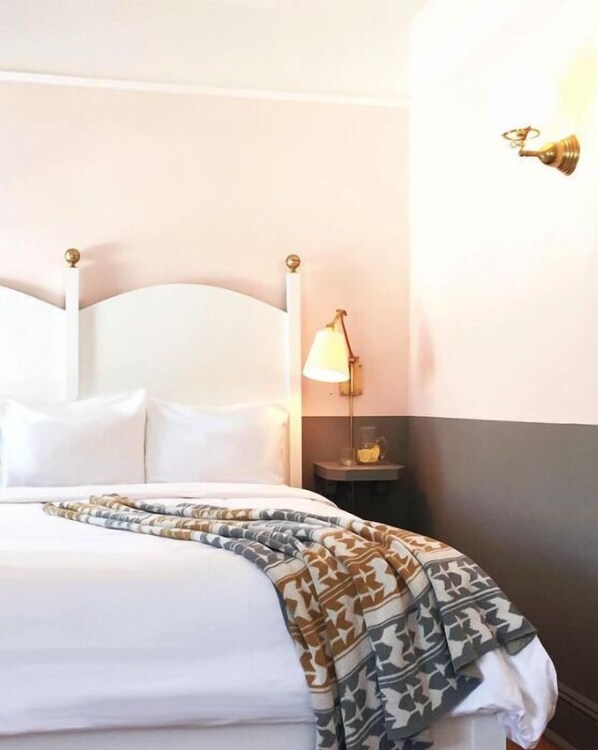 A neatly made bed with a patterned throw blanket, a bedside lamp, and a small table with a glass container.