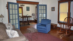 Un saló amb un otomà blau, una cadira d'oscill·lar de fusta i un sofà amb coixins florals.