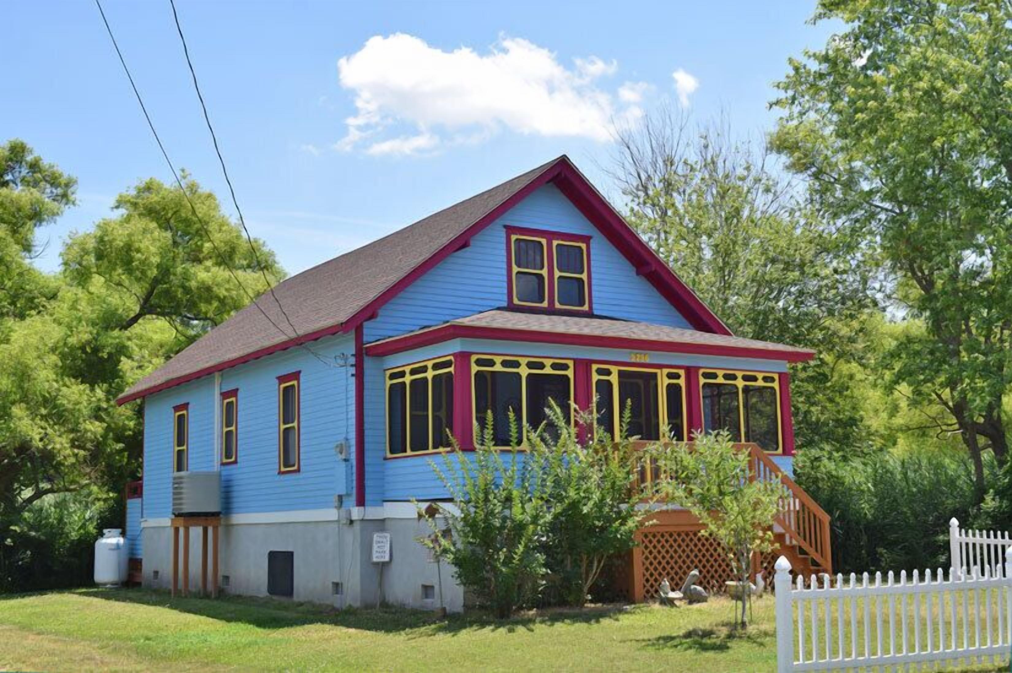 Une maison à deux étages, avec une façade bleue, des bordures rouges et des encadrements de fenêtres jaunes.