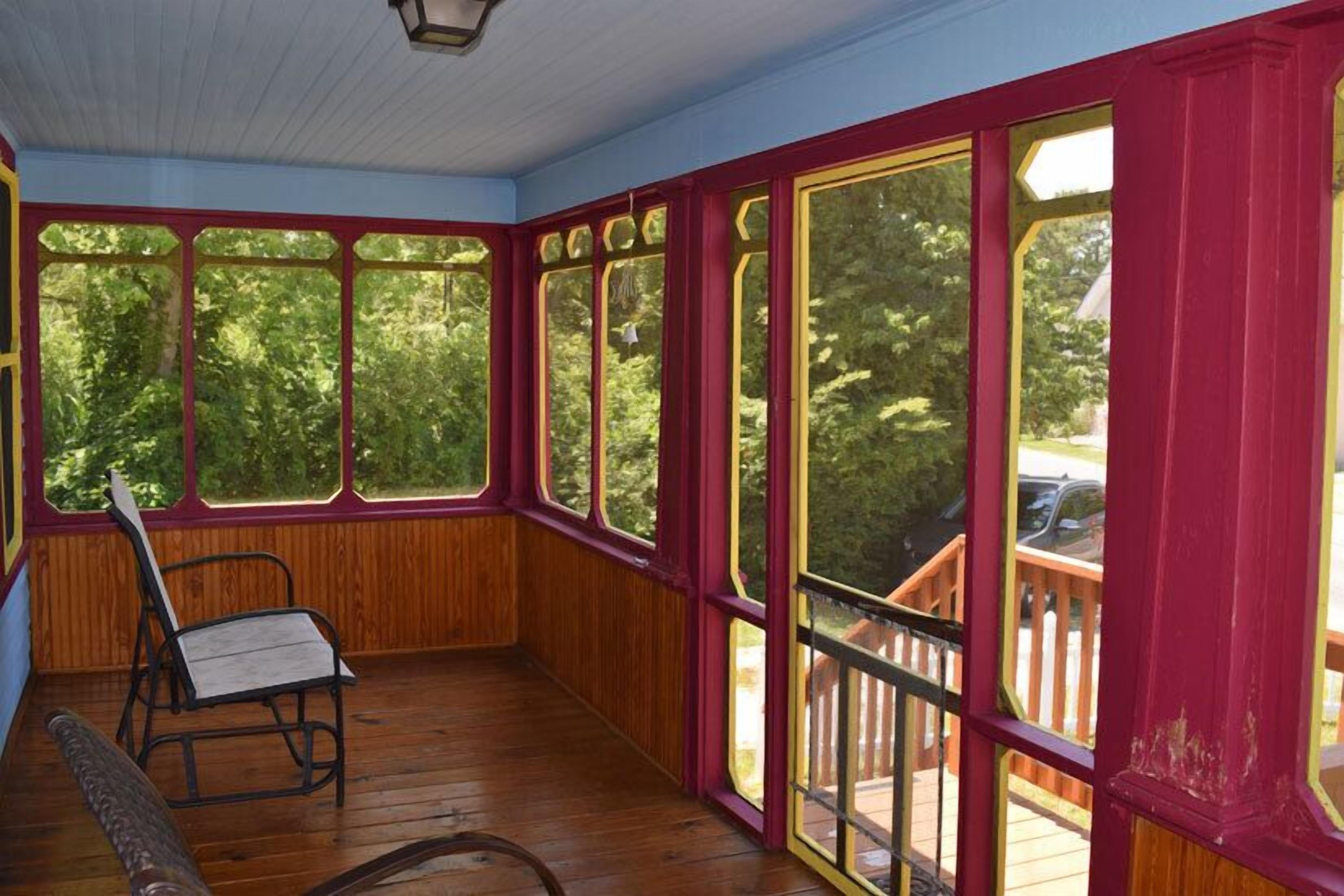 Un porche cubierto con piso de madera y ventanas grandes con detalles en rojo.