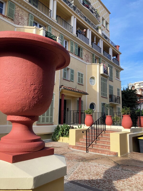 A multi-story building with balconies, a large red urn, and potted plants.
