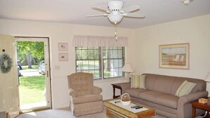 Una sala de estar con un sillón color beige, un sofá marrón, una mesa de centro de madera y un ventilador de techo.