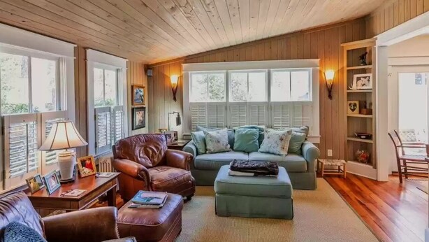 Uma sala de estar aconchegante com tetto de madeira, uma poltrona de couro, um sofá e uma estante de livros.
