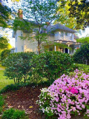 Situated in a peaceful garden, this traditional home features a prominent chimney and a symmetrical facade surrounded by lush greenery.