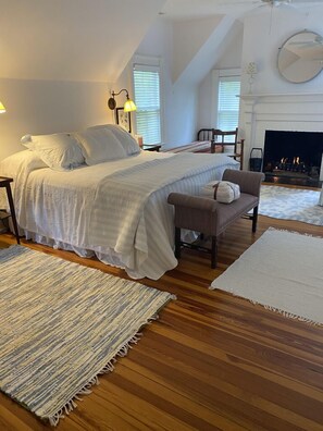 Relax in this serene bedroom with a large bed, a bench, and a chair, accompanied by a fireplace.