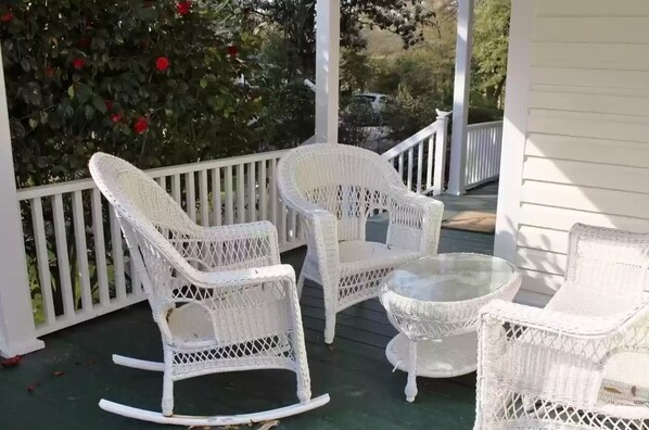 Relax in a serene outdoor seating area with a wicker furniture set, surrounded by lush greenery and vibrant flowers.