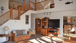 Uma sala de estar ampla com escada de madeira, um sofá, uma mesa de centro e uma televisão.