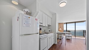 A compact kitchen with white appliances, a dining area, and a balcony with a view. - Carolina Reef 804 - Ocean Front 1 Bedroom Unit - Great Views (North Myrtle Beach)
