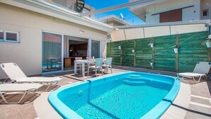 Une piscine avec des chaises longues, un espace repas et un mur végétal.