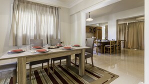 Un coin repas avec une table en bois dressée pour quatre personnes, un tapis à rayures et une cuisine visible au fond.
