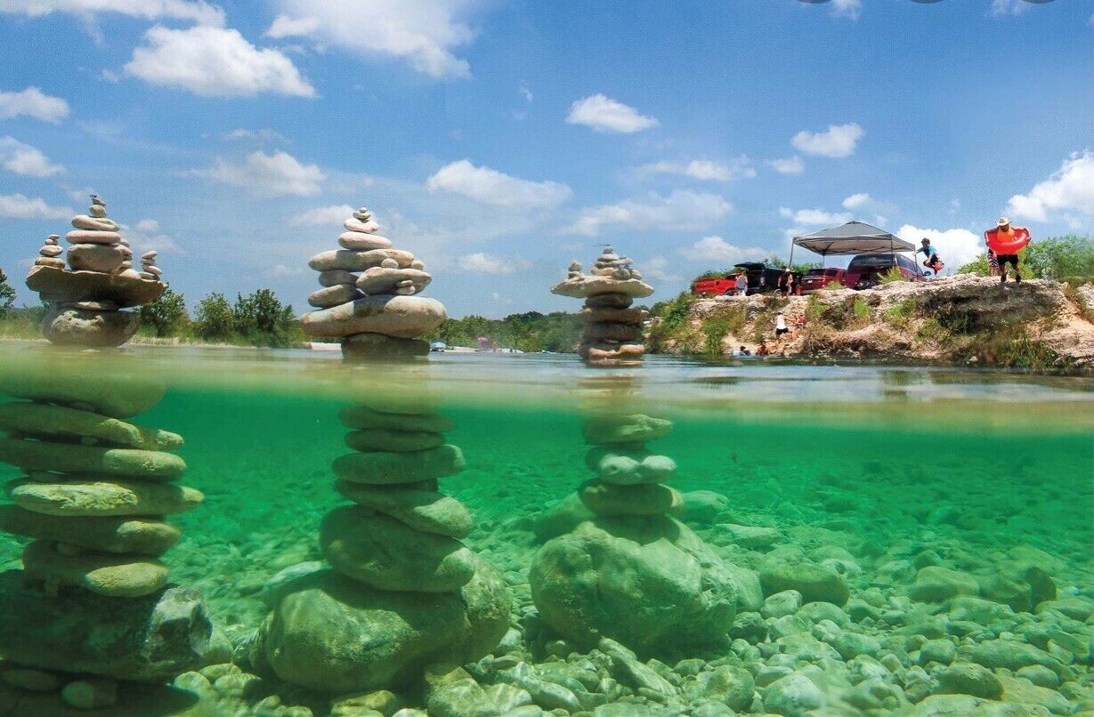 A clear river with rock stacks and a campsite with tents and people.