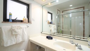 Une salle de bain avec un grand miroir, un lavabo blanc et une fenêtre au-dessus du plan de travail.