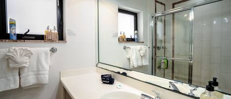 A bathroom with a large mirror, a sink, and a shower. There are towels hanging on the wall and toiletries on the counter.
