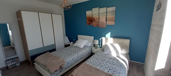 A bedroom with two beds, a wardrobe, and a wall-mounted artwork.