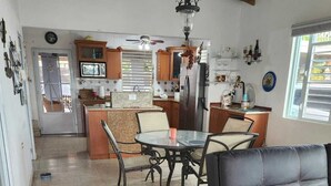 A spacious living area with a black leather sofa, a glass-top dining table, and a kitchen in the background.