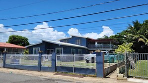 A two-story residential building with a red roof, white picket fence, and a gated driveway.