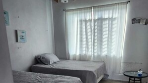A small, clean room with two single beds, a small table, and a window with curtains.