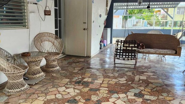 A covered outdoor area with a mosaic floor, wicker furniture, and a wooden ceiling.