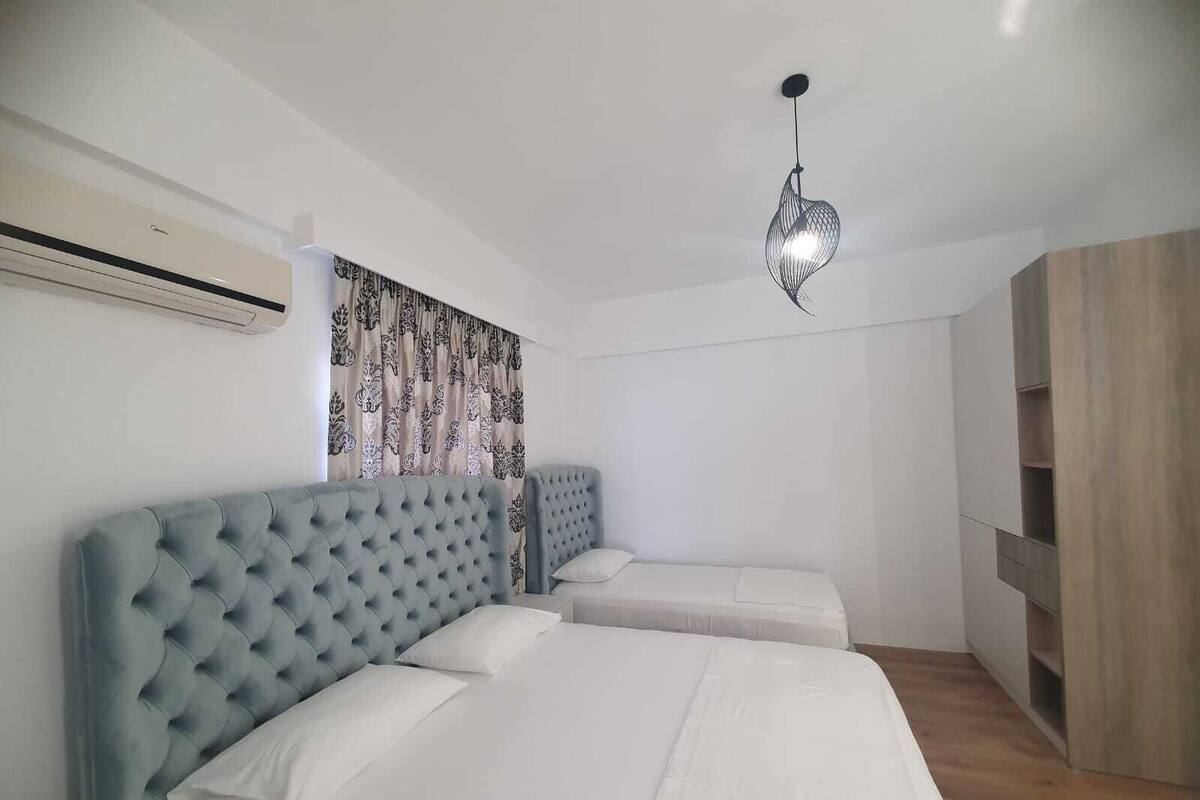A bedroom with two beds, a modern pendant light, a wardrobe, and an air conditioning unit.