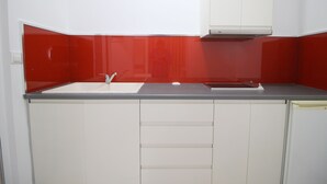 Una cocina con un lavamanos blanco, salpicadero rojo y armarios blancos.