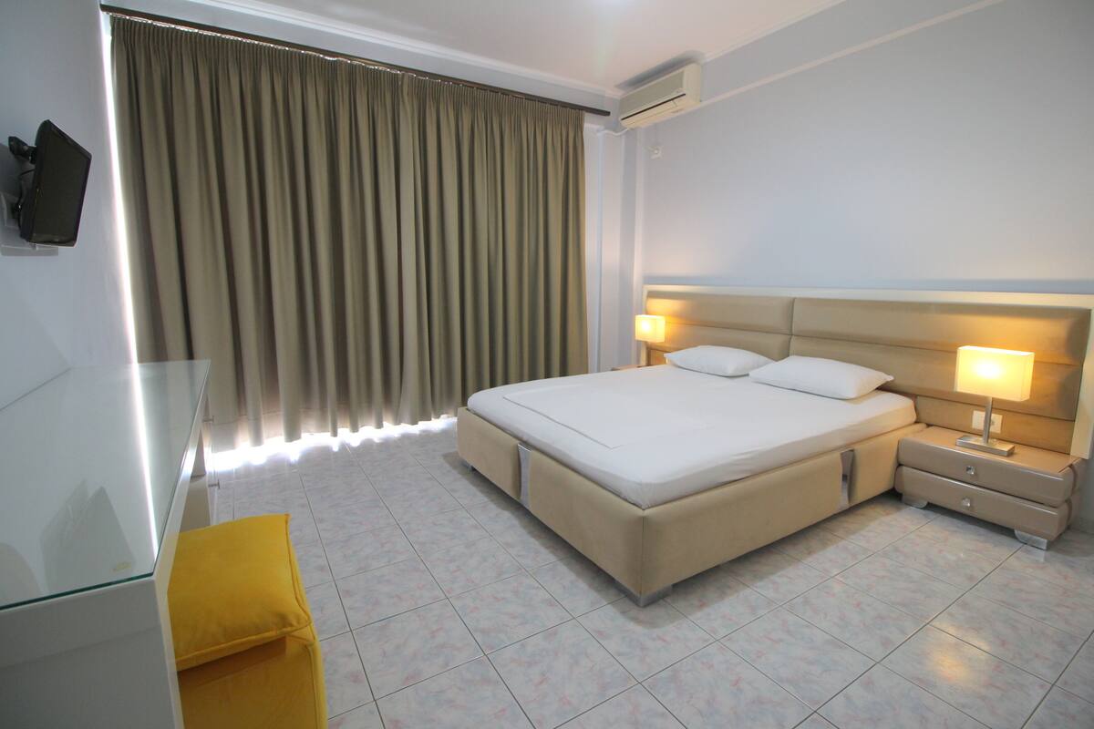 A hotel room with a large bed, bedside lamps, a flat-screen TV, and a yellow chair.