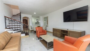 A modern living room with a staircase, leather sofas, a flat-screen TV, and a wooden cabinet. - Beach Front Villa Diamante at Tesoro Ixtapa (Ixtapa Zihuatanejo)