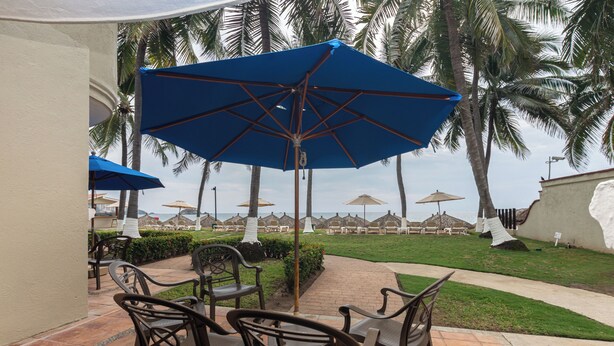 A patio area with outdoor seating and umbrellas, surrounded by palm trees and a view of the ocean. - Beach Front Villa Diamante at Tesoro Ixtapa (Ixtapa Zihuatanejo)