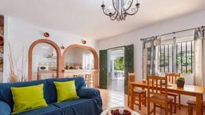 Een woonkamer met een blauwe bank, een eettafel met stoelen, en een keuken die door een open deur zichtbaar is.