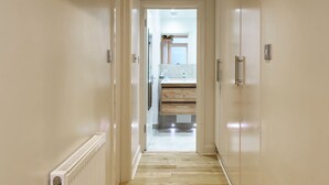 A hallway leading to a bathroom with a wooden floor, white walls, and a visible radiator. - Fantastically Located 2BDR Studio in Kennington (London)