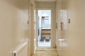 A hallway leading to a bathroom with a wooden floor, white walls, and a visible radiator. - Fantastically Located 2BDR Studio in Kennington (London)