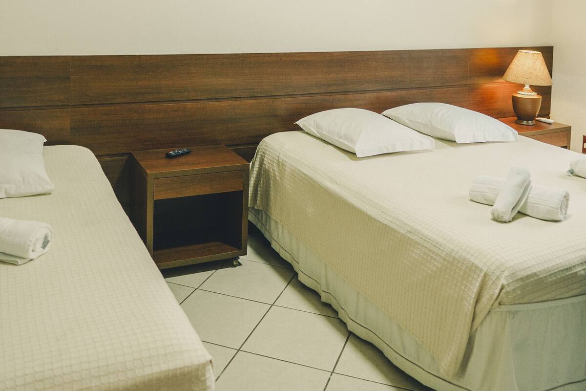 Ein Hotelzimmer mit zwei Einzelbetten, einem Holzkopfende, einem Nachttisch mit Lampe sowie einer Wandklimaanlage.