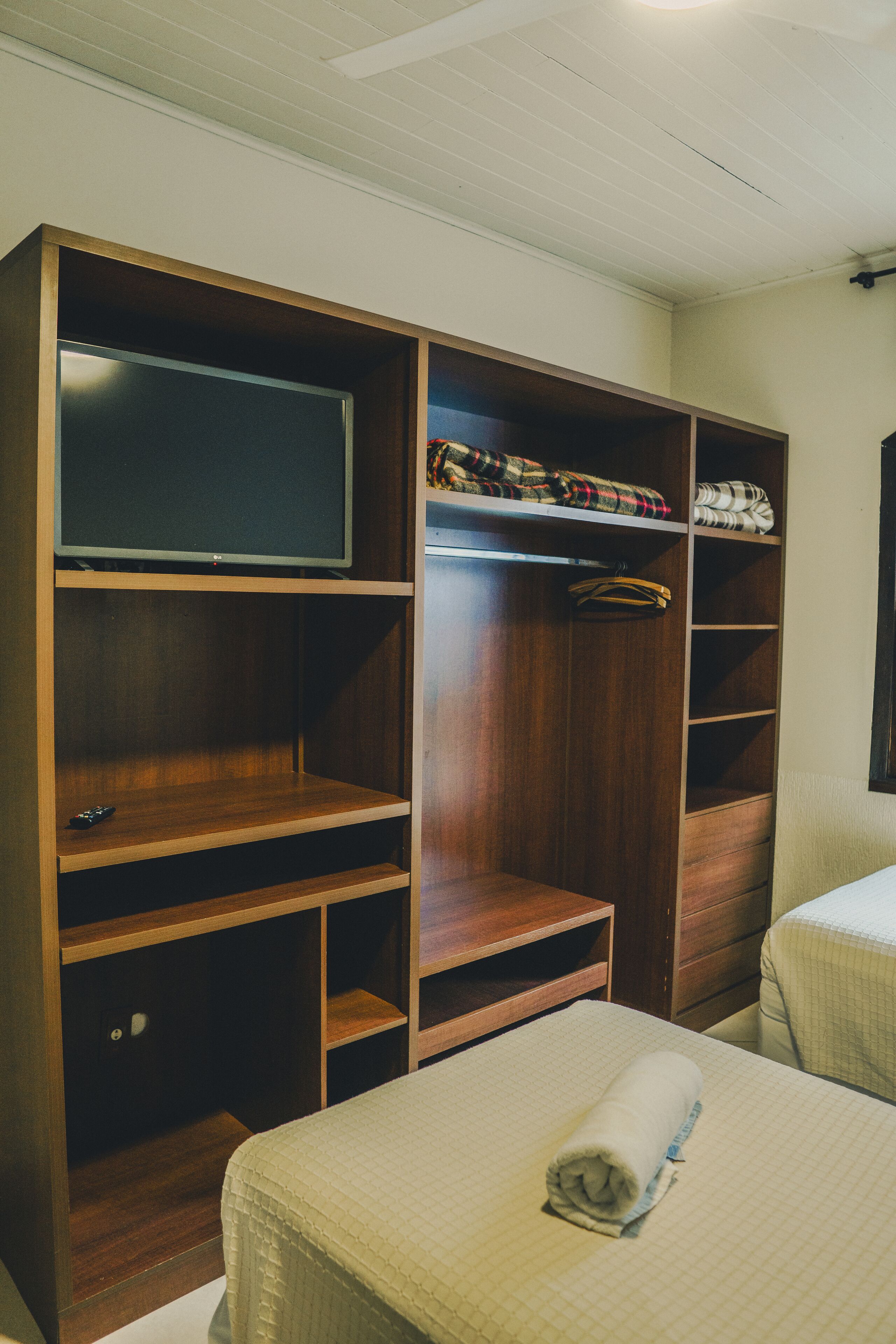 A hotel room with a wooden wardrobe, a television, and a neatly made bed.