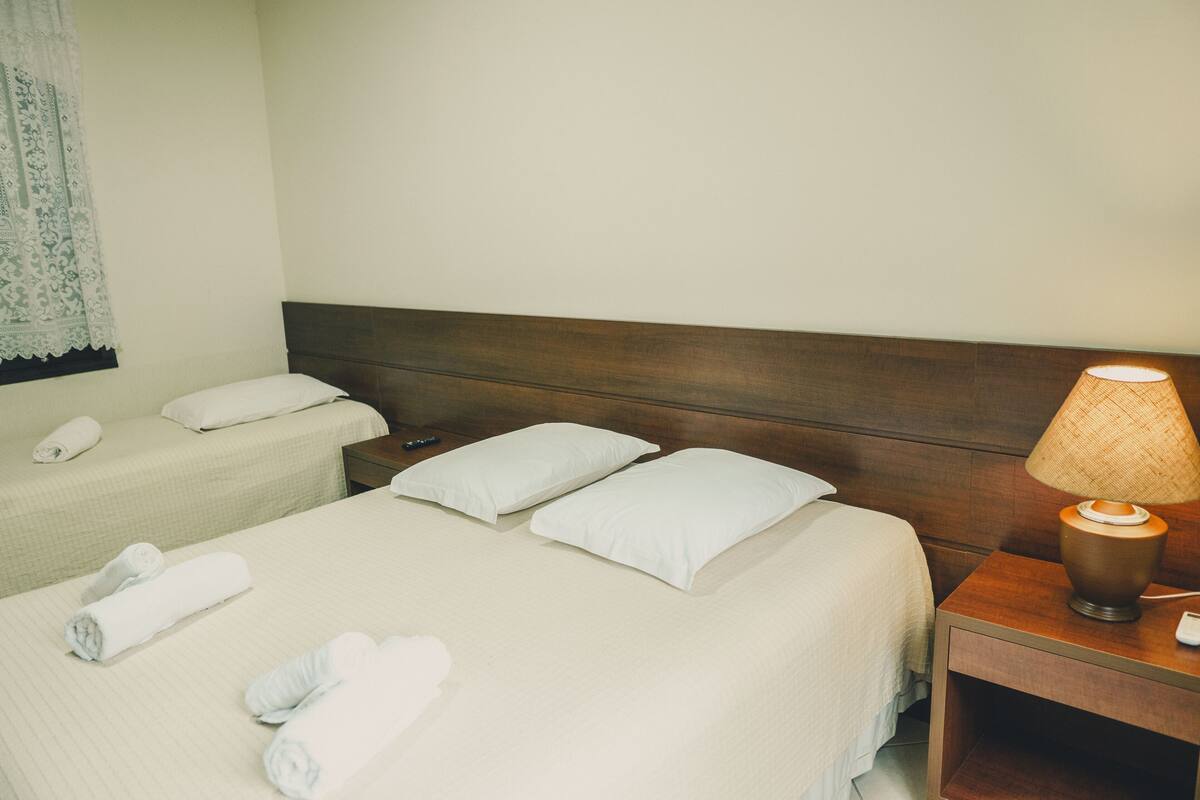 Ein Hotelzimmer mit zwei Betten, beide mit weißen Leinen und Kissen, einem Nachttisch mit einer Lampe und einer Fernbedienung auf dem linken Bett.