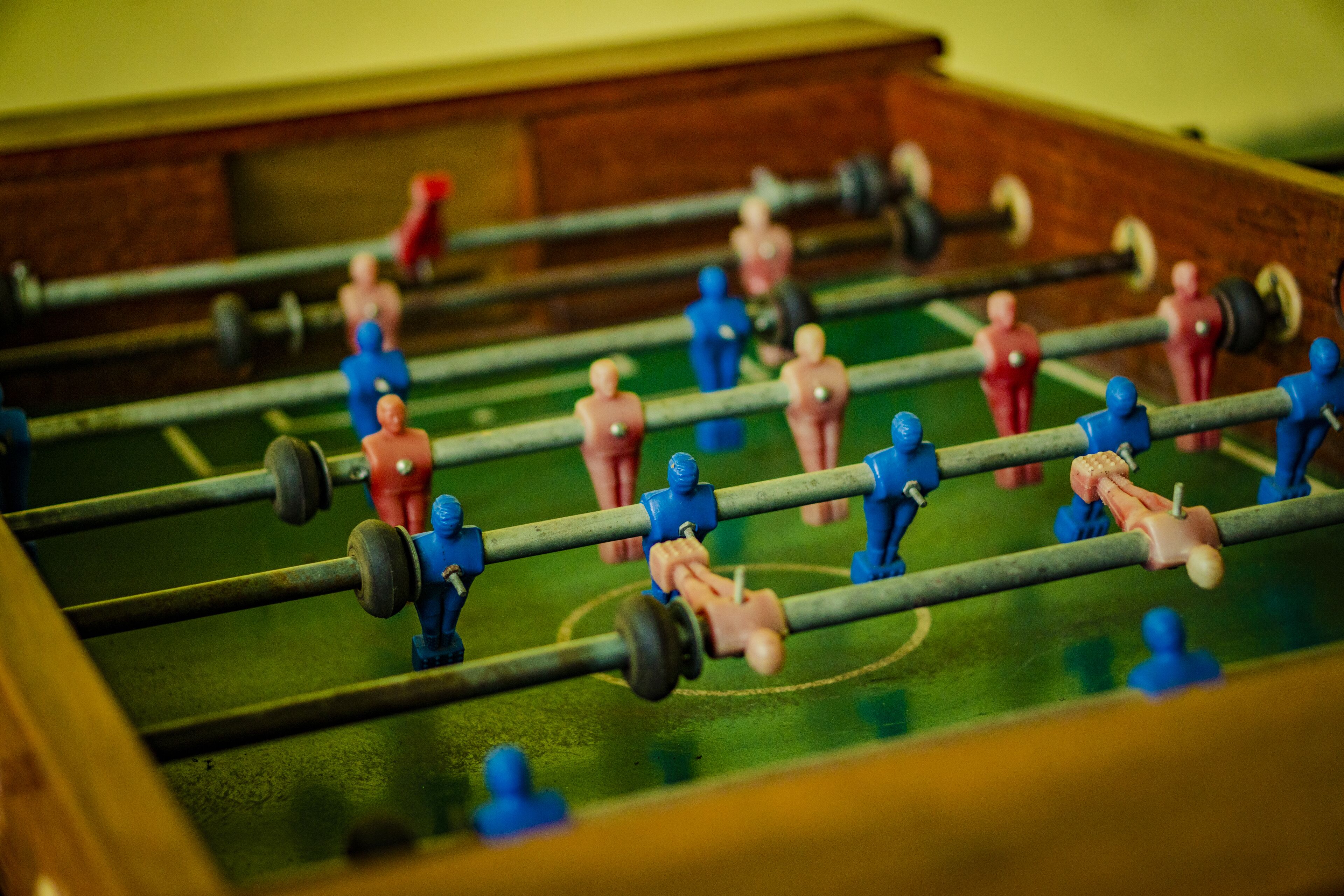 A close-up of a foosball table with figures in blue and red, and a wooden table frame.