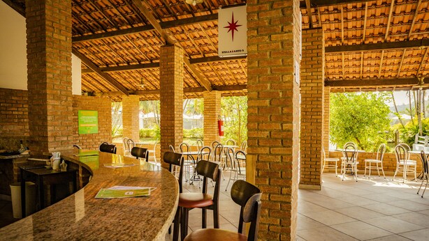 A restaurant with a brick interior, a counter with stools, and a view of greenery outside. - Hotel Fazenda Ramon (Sao Lourenco)