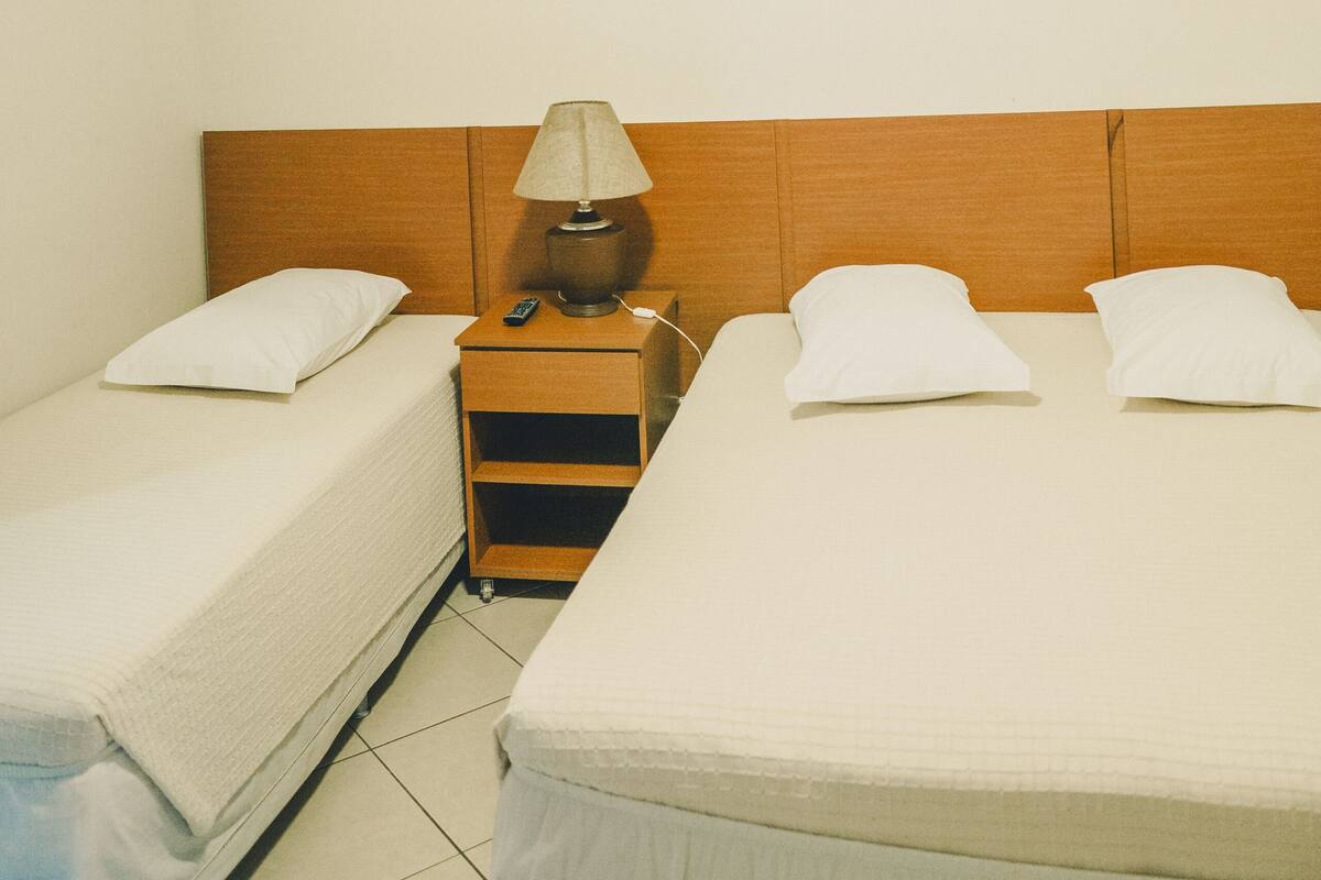 Ein Hotelzimmer mit zwei Einzelbetten, einem hölzernen Kopfteil, einem Nachttisch mit Lampe und einem Deckenventilator.