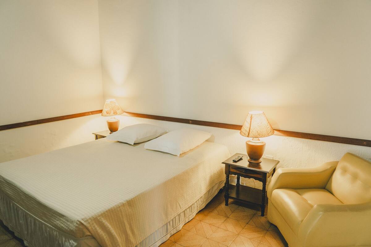 Ein Hotelzimmer mit einem Bett, zwei Nachttischen, einer Lampe, einem Sessel und einem Beistelltisch.