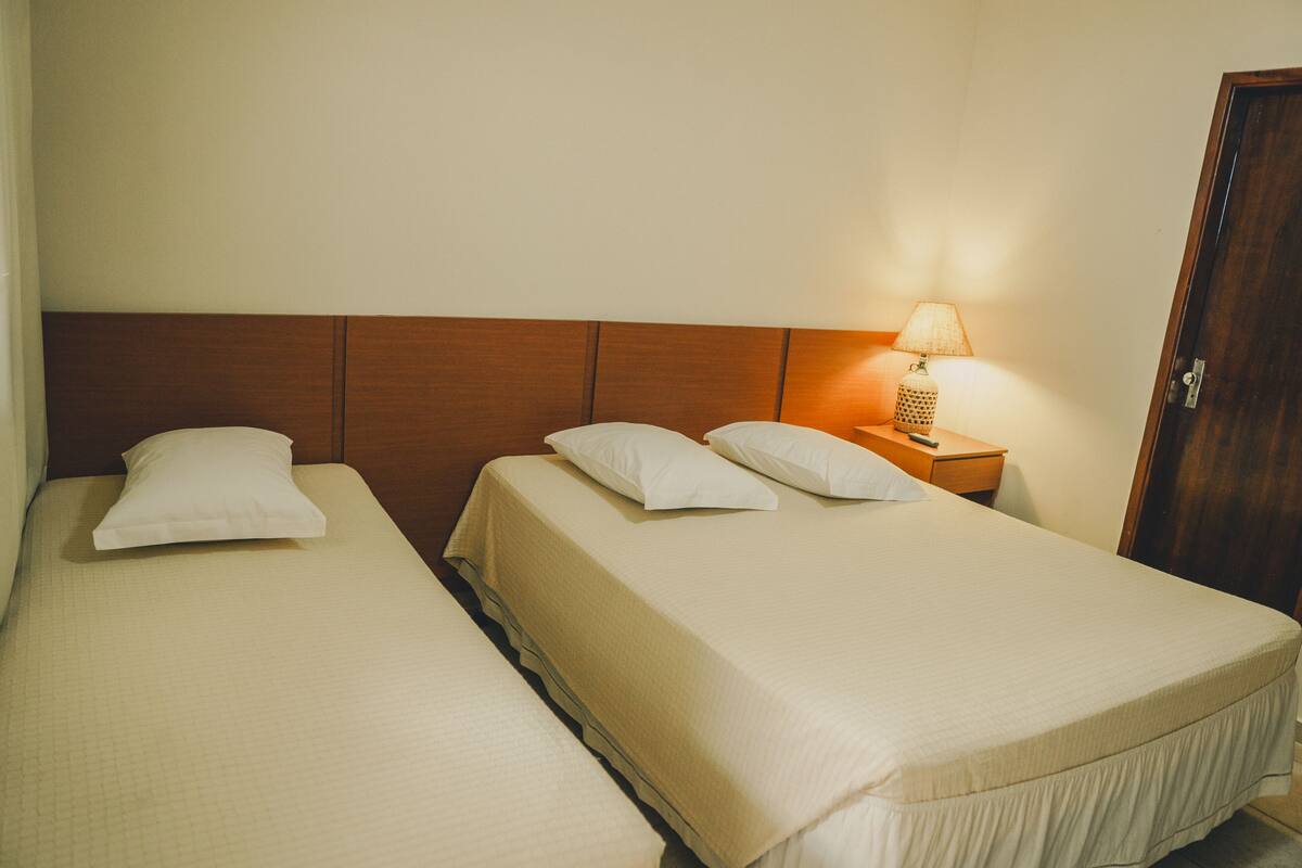 Ein Hotelzimmer mit zwei Einzelbetten, einem hölzernen Kopfteil, einem Nachttisch mit Lampe und einer Tür.