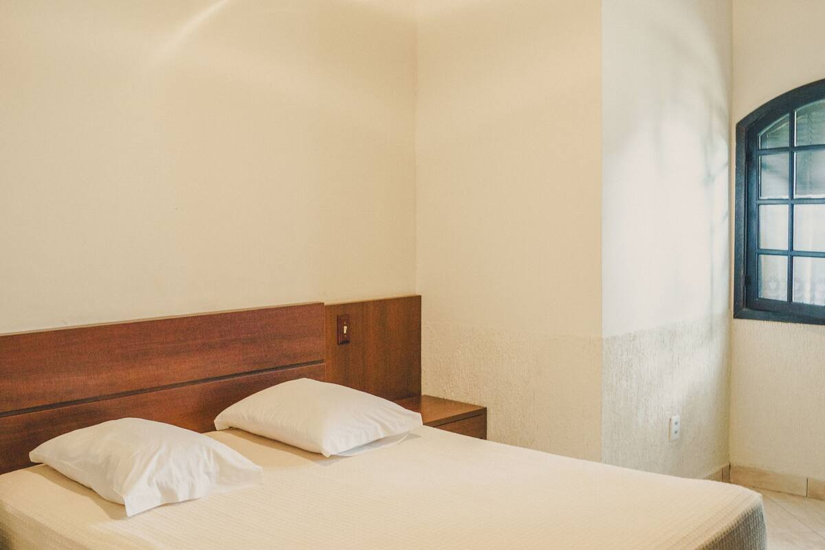 Ein Schlafzimmer mit hölzernem Kopfteil, zwei Einzelbetten, einem Nachttisch, einem Deckenventilator und einem Fenster mit Blick.