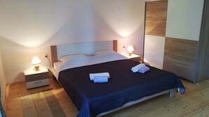 Een net opgemaakt bed met een donkerblauwe dekbedovertrek, twee nachtkastjes met lampen, en een houten garderobe.
