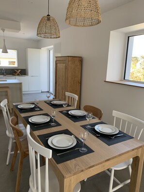 A dining area with a long wooden table set for four, white chairs, and two woven pendant lights. - Maison Avec Piscine Intérieure Sainte-marine à 300m de la Plage (Combrit Sainte-Marine)