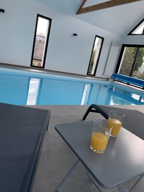 A poolside area with a table and two glasses of orange juice, a bench, and a view of the pool. - Maison Avec Piscine Intérieure Sainte-marine à 300m de la Plage (Combrit Sainte-Marine)